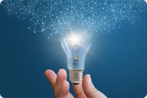 A hand holds a glowing light bulb against a dark blue background. Above, a network of interconnected lines suggests innovation and ideas.